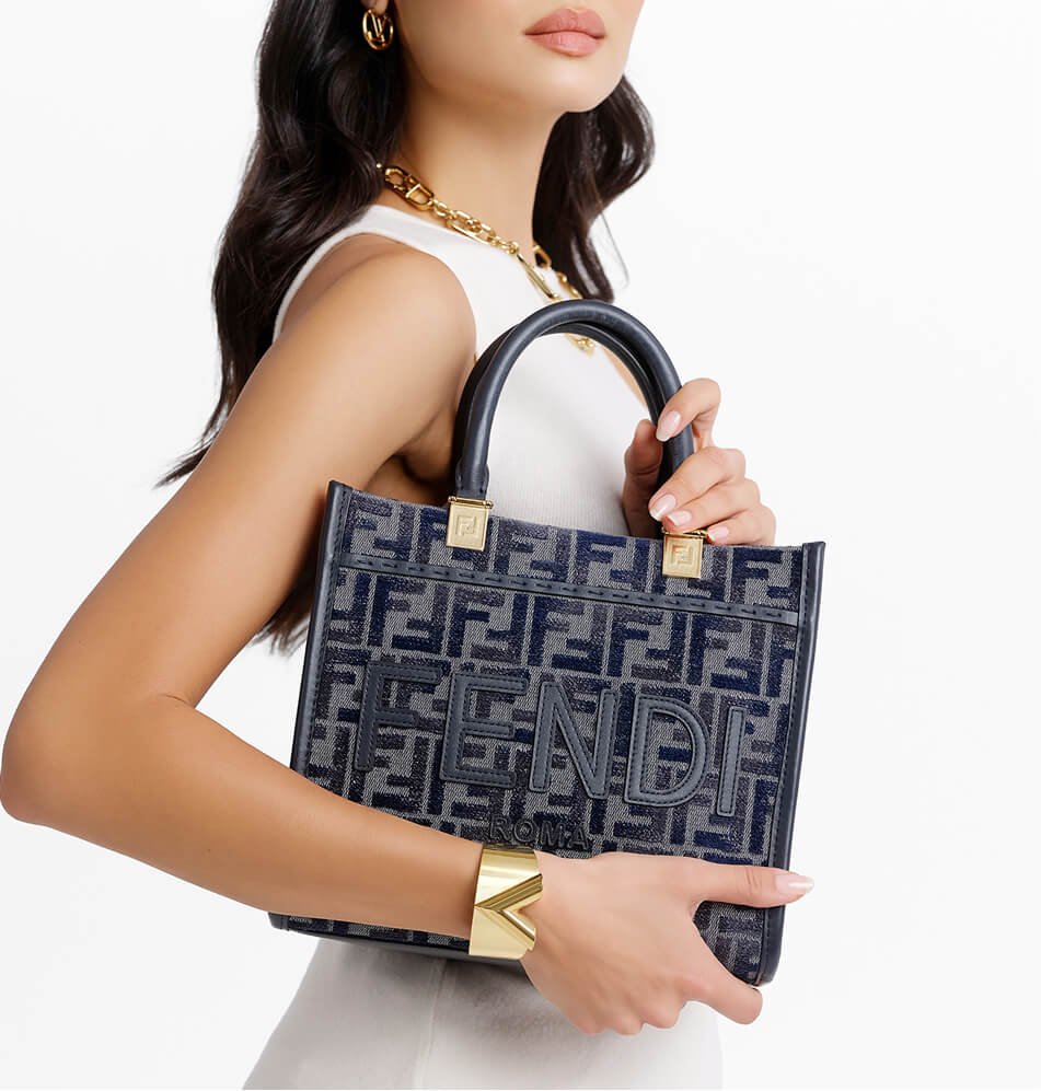 25 a woman holds a fendi handbag with a navy blue and gray monogram pattern and gold tone hardware against a clean white background