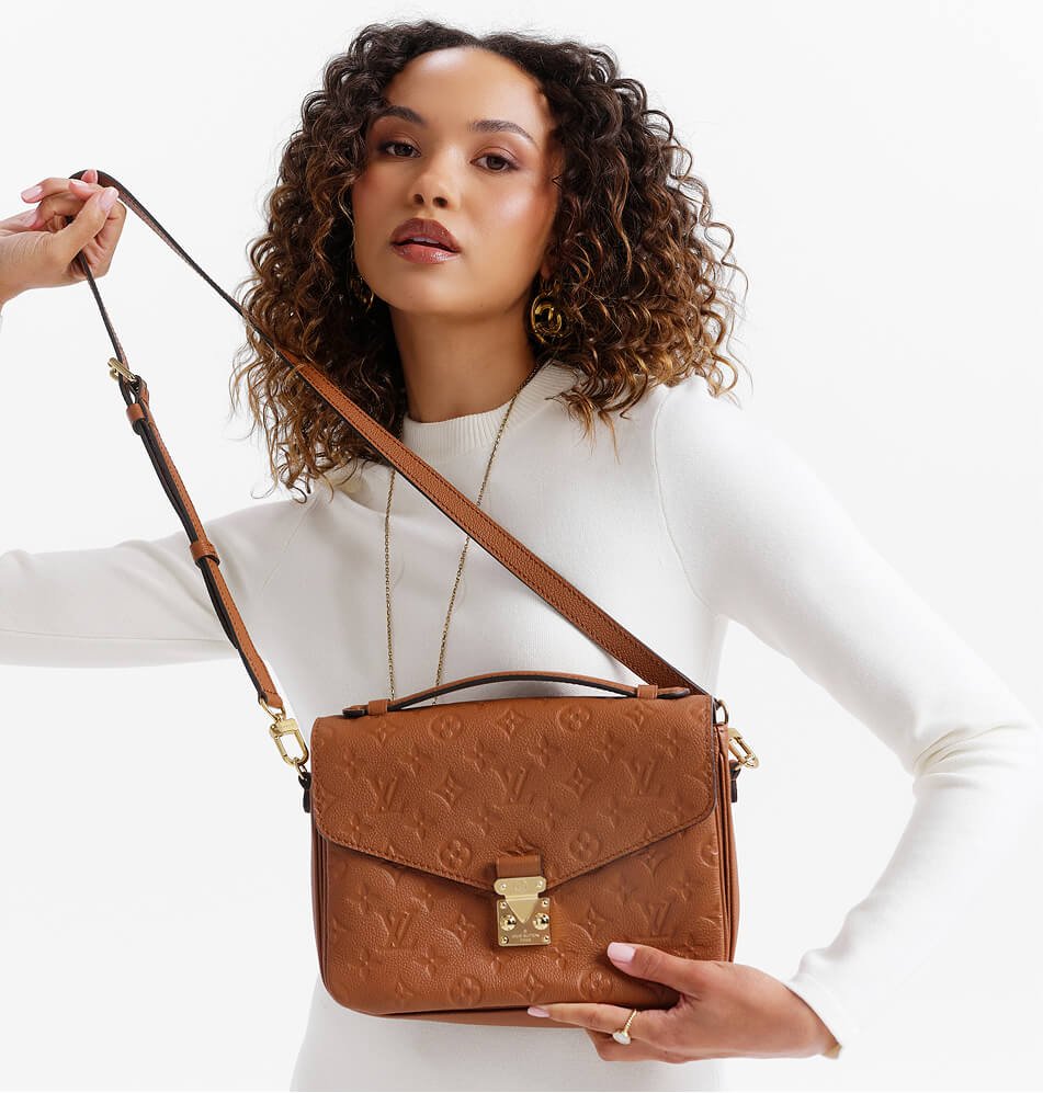 27 a woman wearing a white mock neck top holds a brown embossed leather shoulder bag with a gold clasp and strap against a clean white background